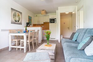 A compact living space with a dining area, kitchenette, and a grey sofa with cushions.