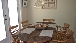 Mesa de jantar redonda de madeira com seis cadeiras, saleiro e pimenteiro, e um quadro com um pássaro na parede.