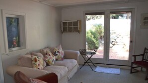 Sala de estar com sofá, mesa pequena, cadeira e porta que dá para uma área externa.