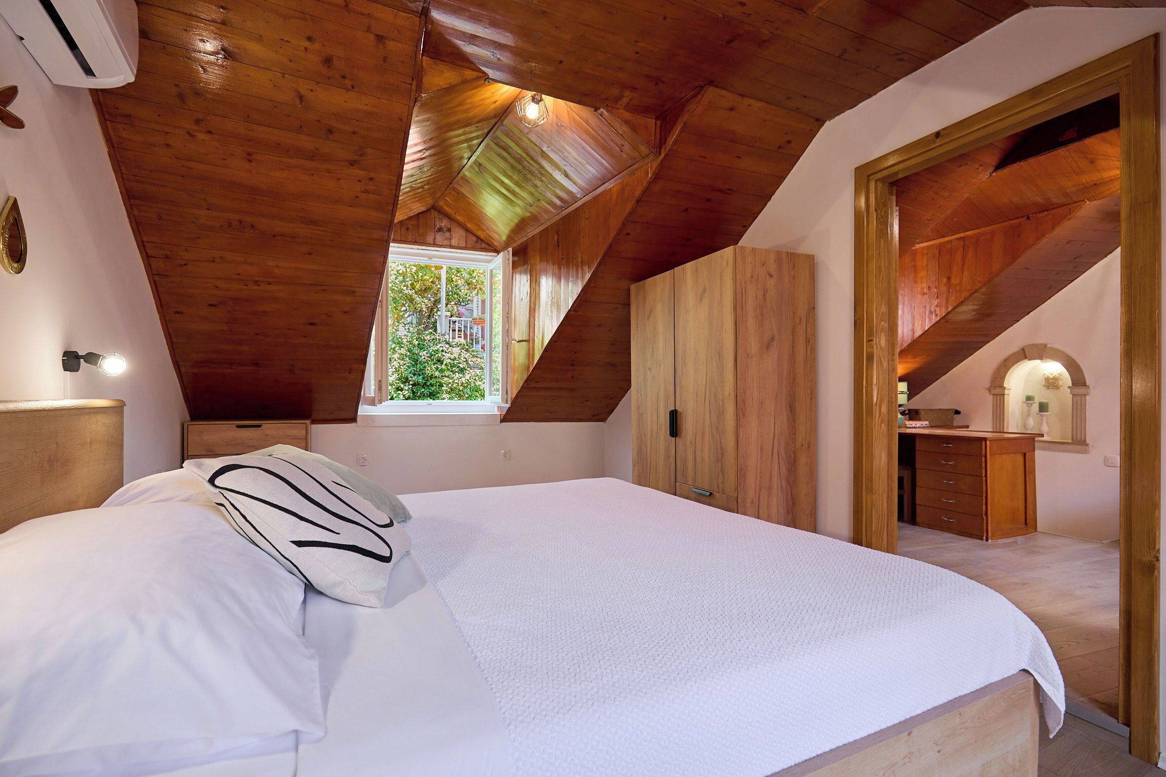 Ein Schlafzimmer mit Holzbalkendecke, einem Bett mit weißer Bettwäsche, einem Fenster und einem Holzschrank.