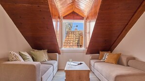 A cozy attic room with wooden beams, two sofas, a coffee table, and a window with a view of a tiled roof. - Hedera Estate, Hedera A6 (Dubrovnik)