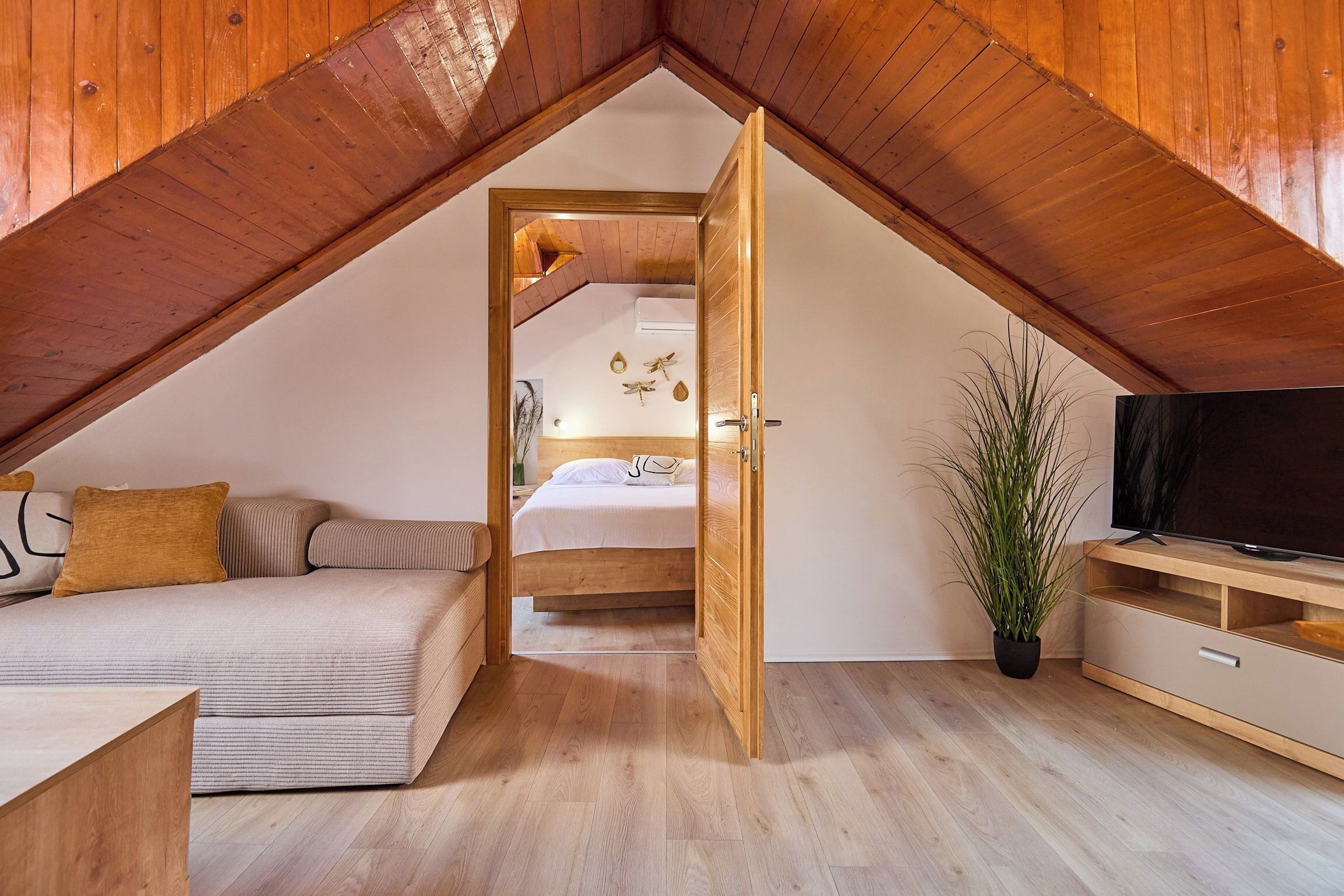 Une chambre confortable située dans les combles, avec un plafond en bois, un lit, un canapé et un téléviseur.