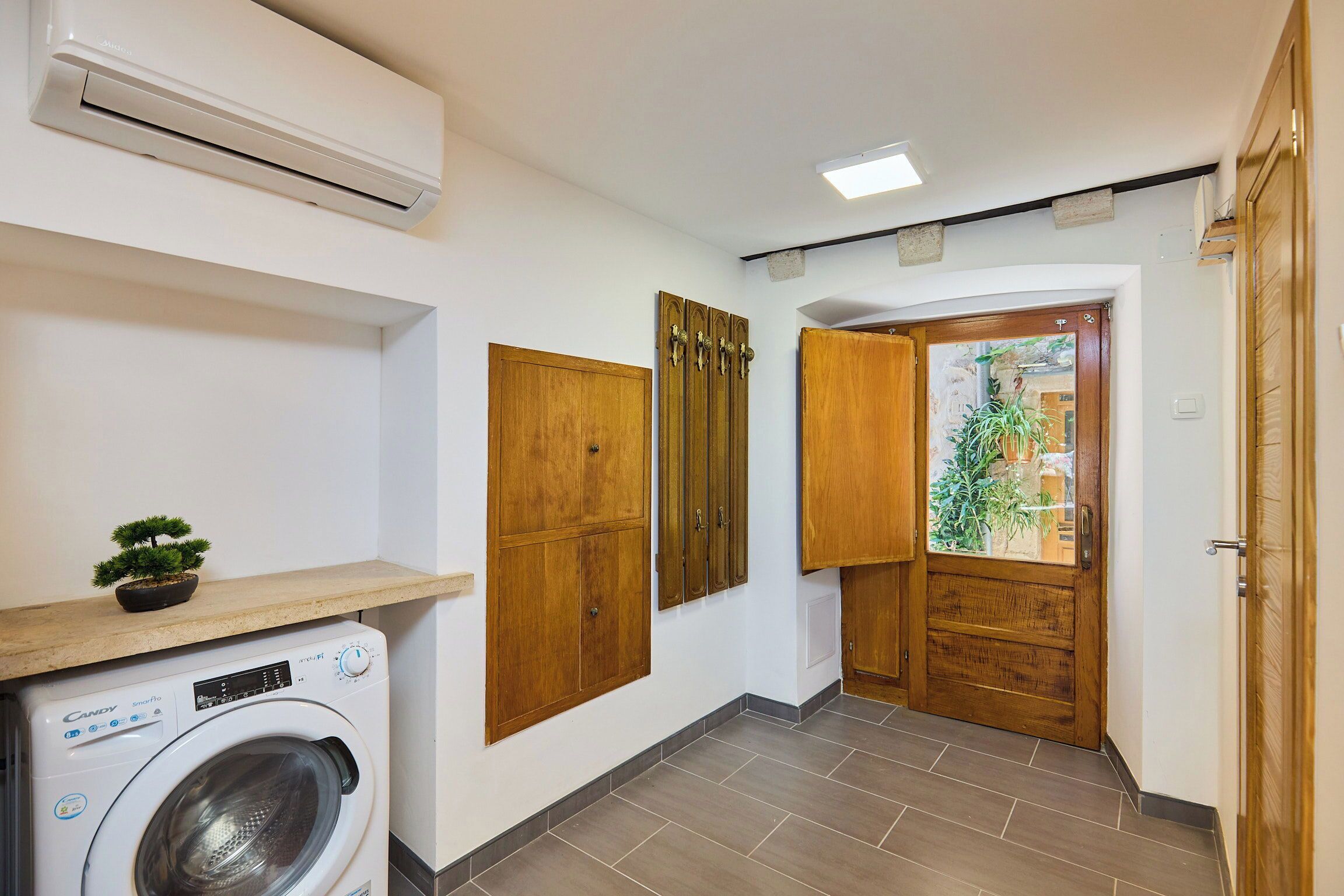 A laundry area with a washing machine, wooden cabinets, and a door leading to a balcony with a view.