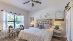 A bedroom with a large bed, two bedside tables with lamps, a ceiling fan, and a window with blinds.