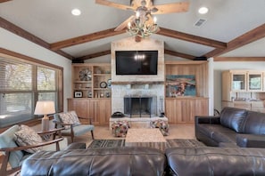 A spacious living room with a stone fireplace, leather sofas, and a ceiling fan. - Ranch Retreat Creek View - Pool Table and Fire Pit (Fredericksburg)
