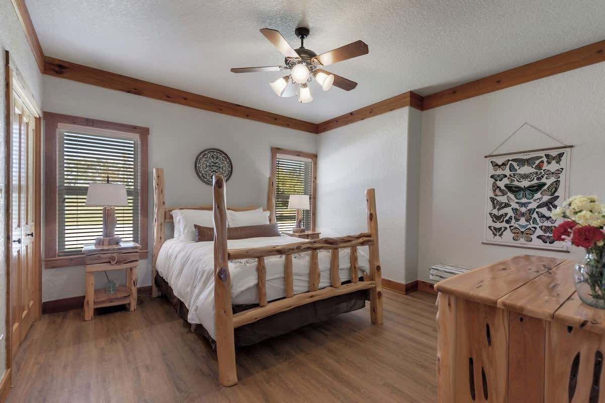 Un dormitorio con una cama de madera, un ventilador de techo y una mesita de noche de madera con una lámpara.