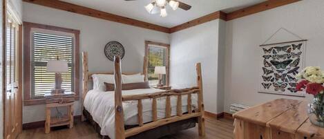 Un dormitorio con una cama de madera, un ventilador de techo y una mesita de noche de madera con una lámpara.