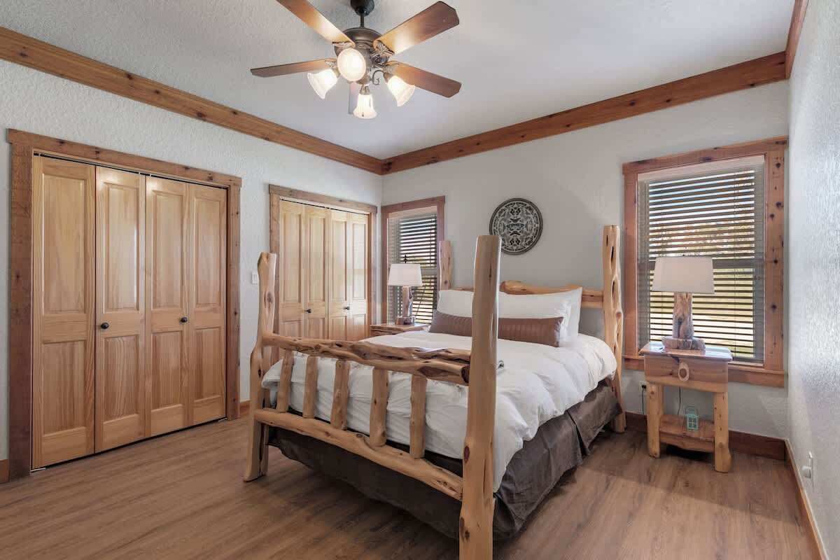 Un dormitorio con cama de madera, ventilador de techo, armarios de madera y ventana con persianas.