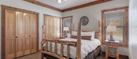 Un dormitorio con cama de madera, ventilador de techo, armarios de madera y ventana con persianas.