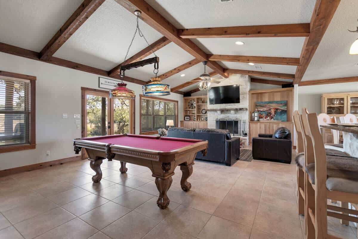 Un vaste espace de vie comprenant une table de billard, des poutres apparentes et une cheminée.