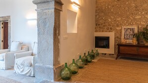 A room with a stone wall, a fireplace, and a row of green bottles. - Agroturisme Subies (Selva)
