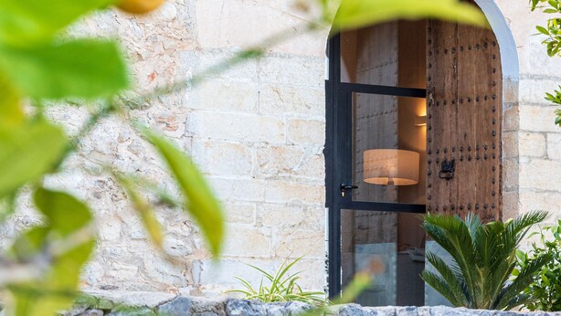 A stone building with a wooden door and green shutters, a balcony with a railing, and a stone wall. - Agroturisme Subies (Selva)