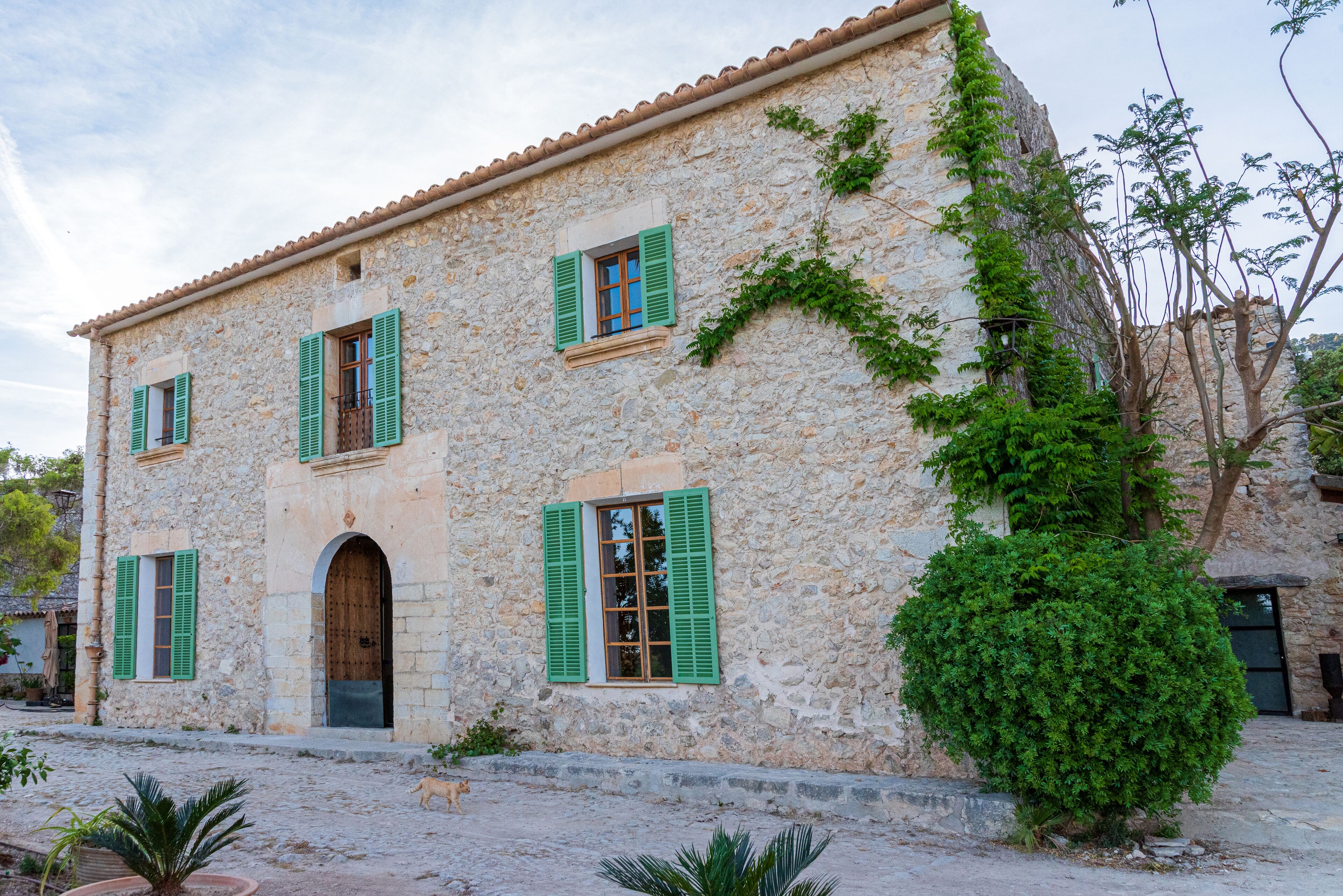 Un bâtiment en pierre avec des volets verts, une porte en bois et un petit jardin.
