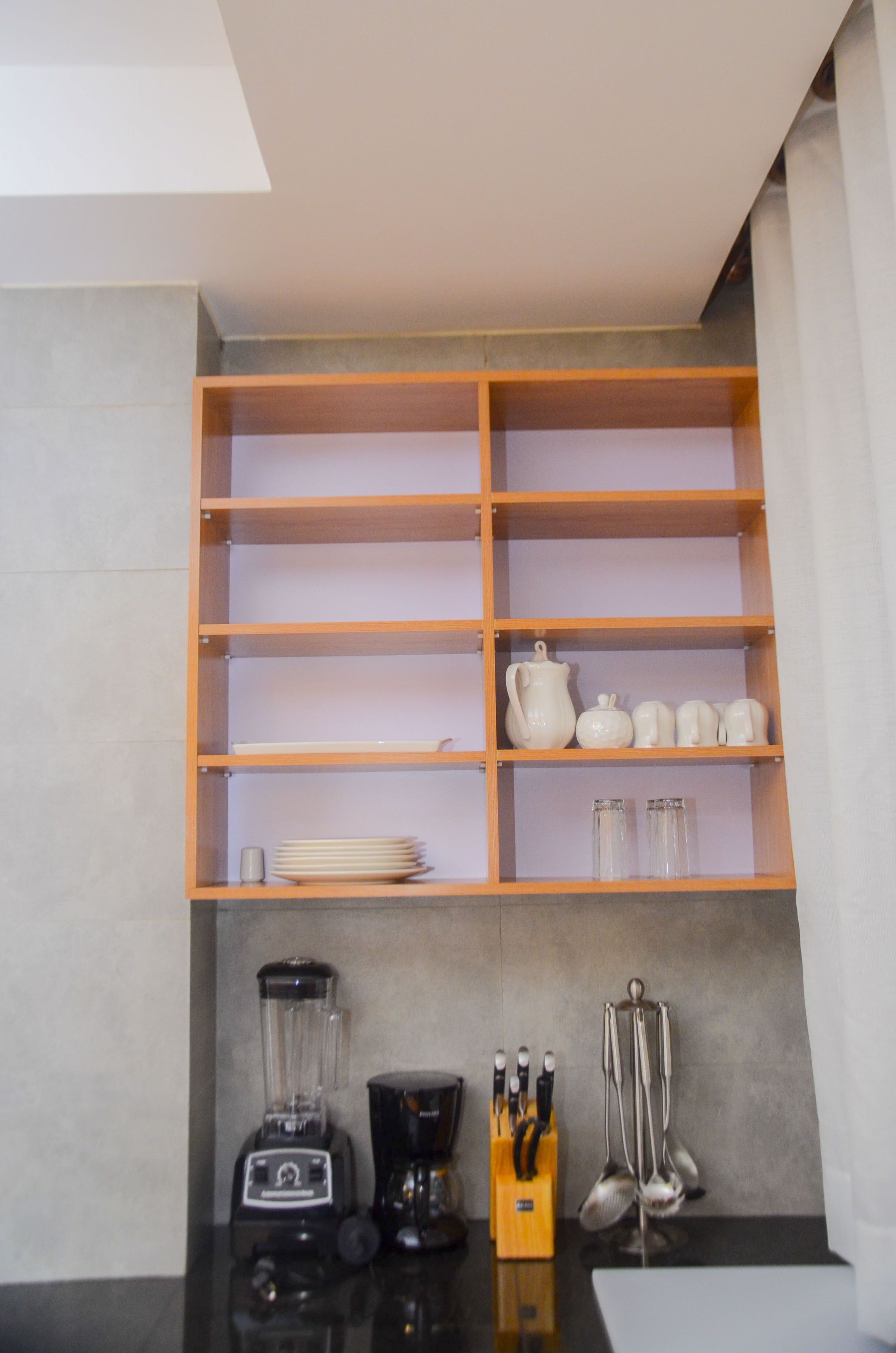 A kitchen with a wooden shelf unit, a blender, a coffee maker, and utensils.