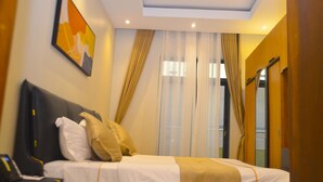 Quarto de hotel com uma cama, uma mesa de cabeceira com telefone, um quadro na parede e uma janela com cortinas.