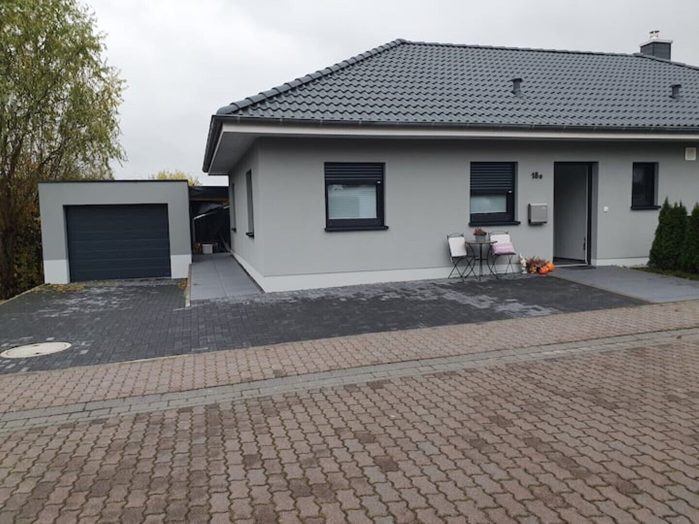 Una casa moderna de dos pisos con fachada gris, techo de tejas y entrada pavimentada.