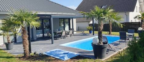 Une maison moderne dotée d’une piscine, d’un patio couvert et de palmiers.