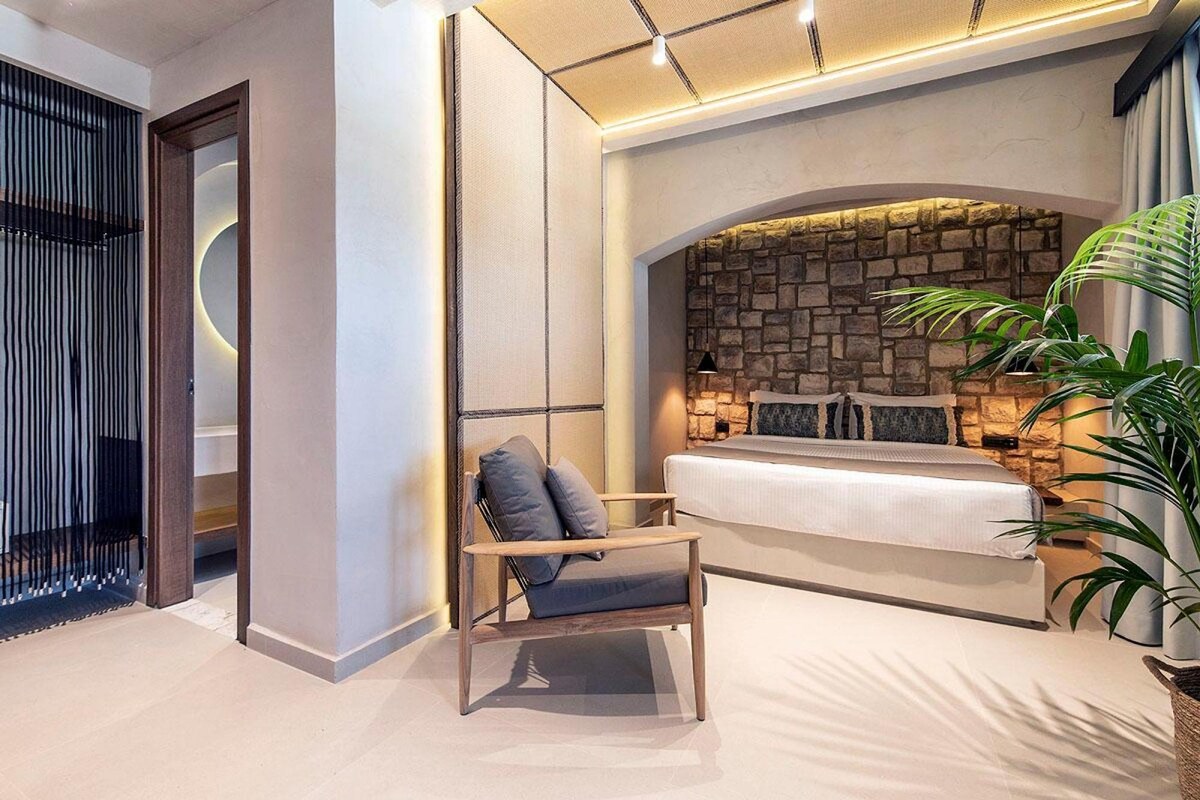 Une chambre moderne avec un mur d’accent en pierre, un lit avec des oreillers, une chaise et une plante en pot.