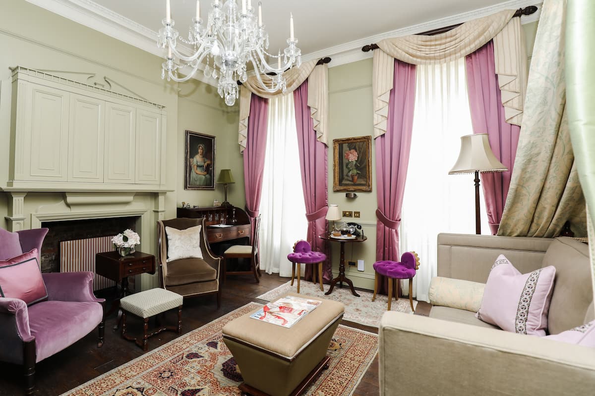 A room with a fireplace, a chandelier, a sofa, a chair, and a table with a lamp.