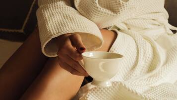 A person in a white bathrobe sitting on a bed with a white bowl.