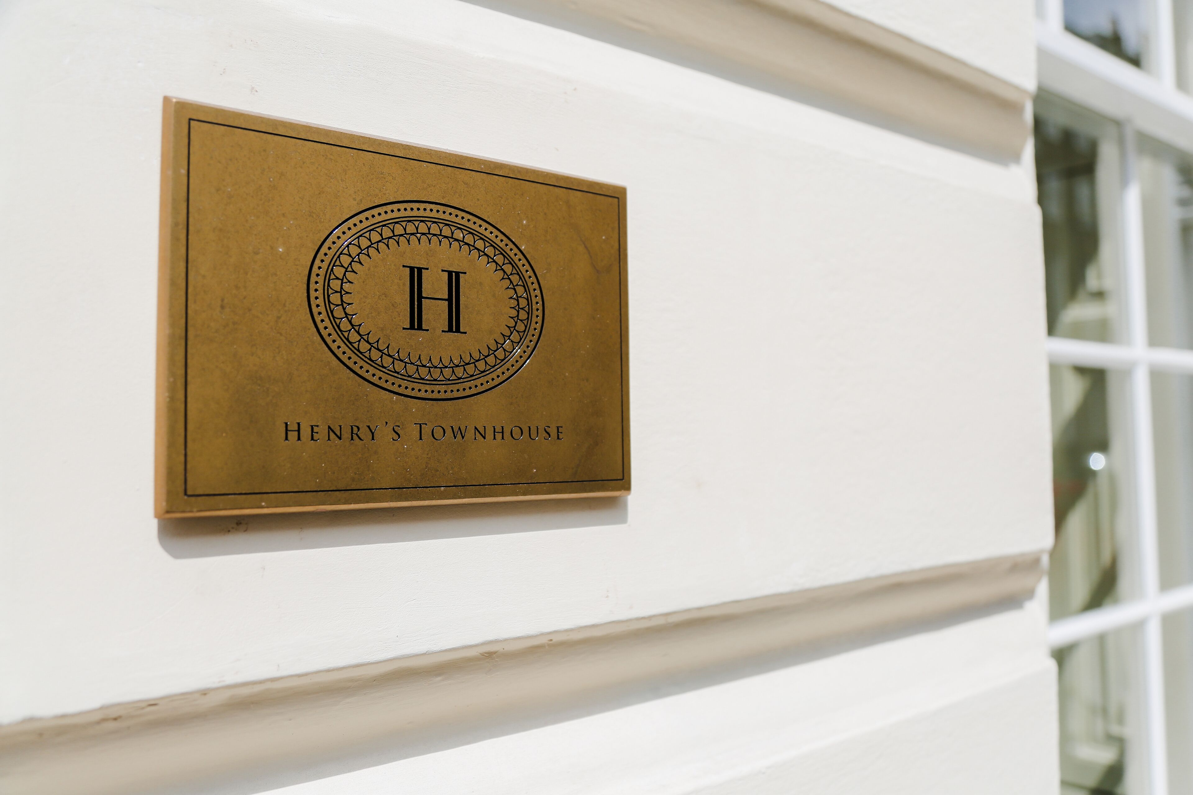 A brass plaque with a monogram and the text "Henry's Townhouse" on a white wall.