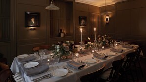 Un comedor formal con una larga mesa dispuesta para una comida, retratos enmarcados en las paredes y luz de velas.