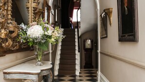 A grand hallway with a checkered floor, a large ornate mirror, a vase of flowers, and a staircase leading to an upper level. - Henry's Townhouse (London)
