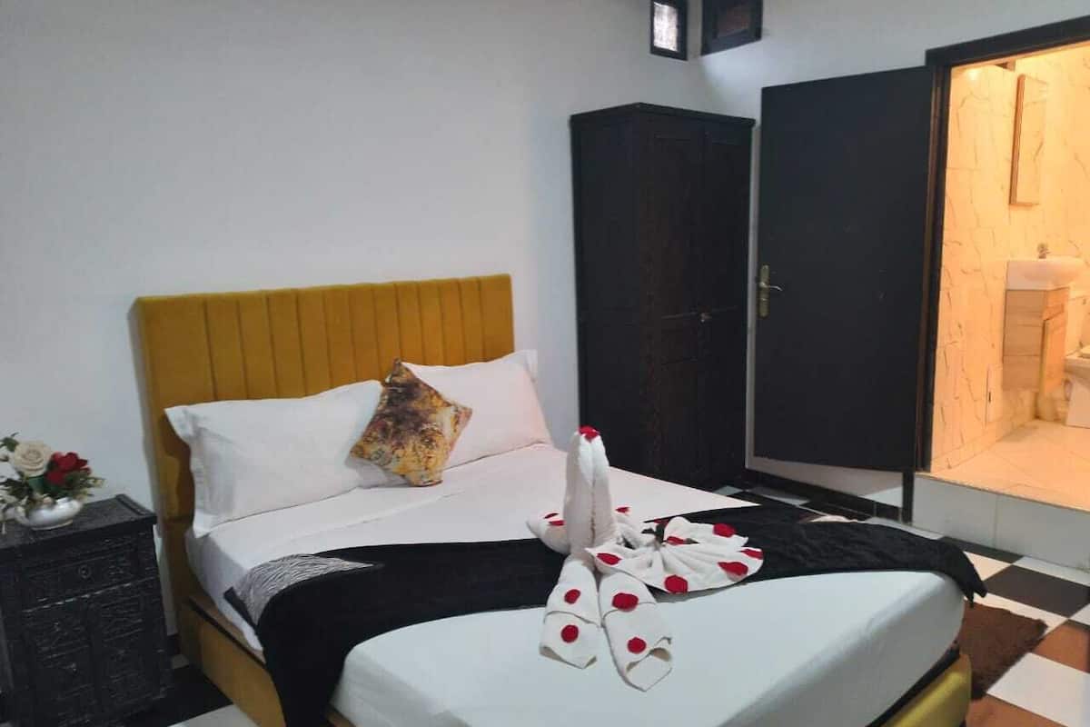 A hotel room with a bed, a wardrobe, and a bathroom visible through an open door.