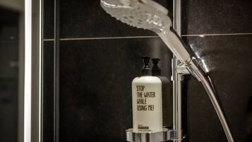 A bathroom with a shower, a soap dispenser, and a tiled wall.