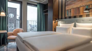 Habitación de hotel con una cama grande, una silla, un escritorio y vistas a la ciudad a través de las ventanas.