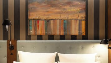 A hotel room with a bed, two bedside lamps, and a cityscape painting on the wall.
