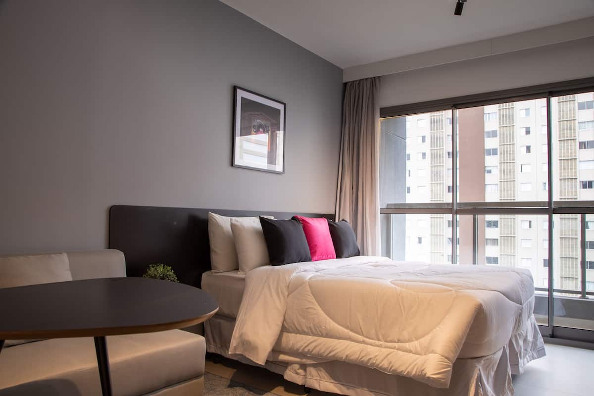 Ein modernes Hotelzimmer mit einem großen Bett, einer Couch, einem kleinen Tisch und einem großen Fenster mit Blick auf die Stadt.