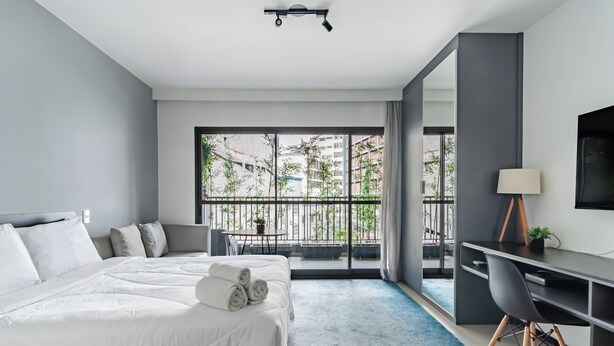 Une chambre d’hôtel moderne dotée d’un grand lit, d’un bureau et d’un balcon offrant une vue sur la ville.