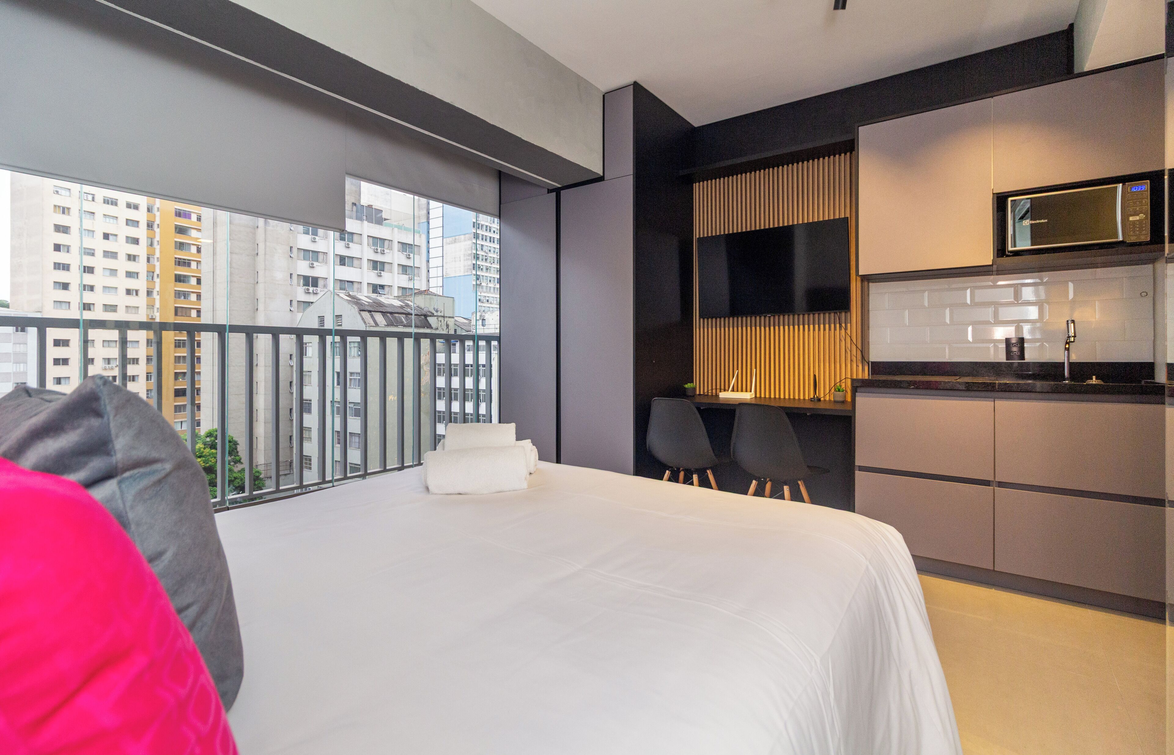 Een moderne hotelkamer met een groot bed, een kitchenette en een balkon met uitzicht op de stad.
