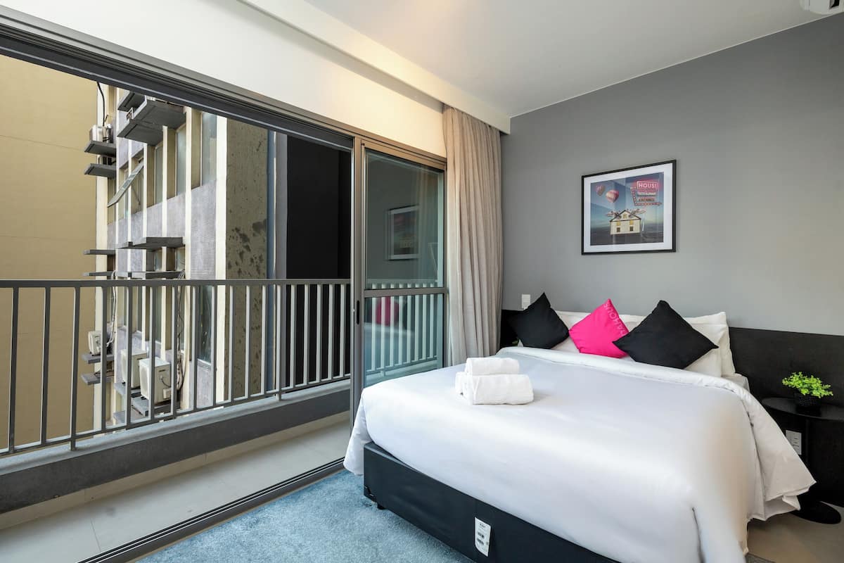 Ein Hotelzimmer mit Bett, Nachttisch, einem gerahmten Bild an der Wand und Blick auf den Balkon.