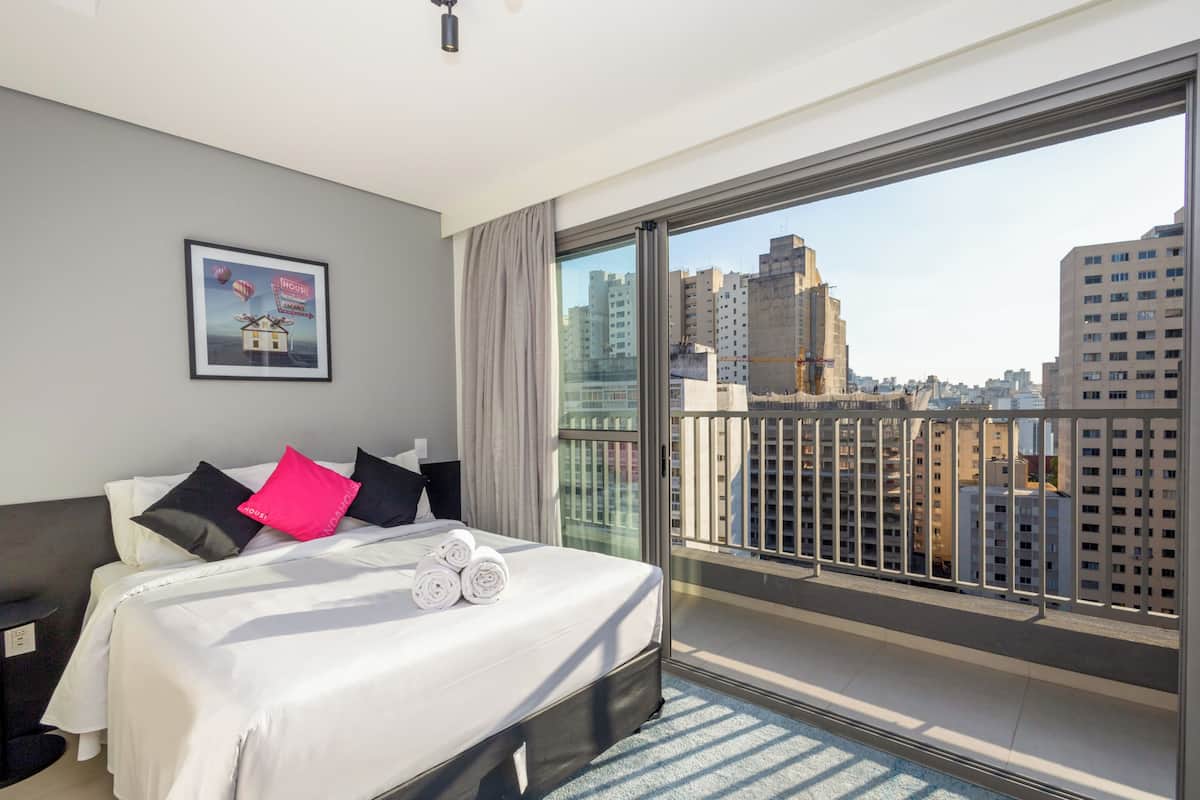 Ein modernes Hotelzimmer mit einem großen Bett, einem Balkon mit Stadtblick und einem gerahmten Poster an der Wand.