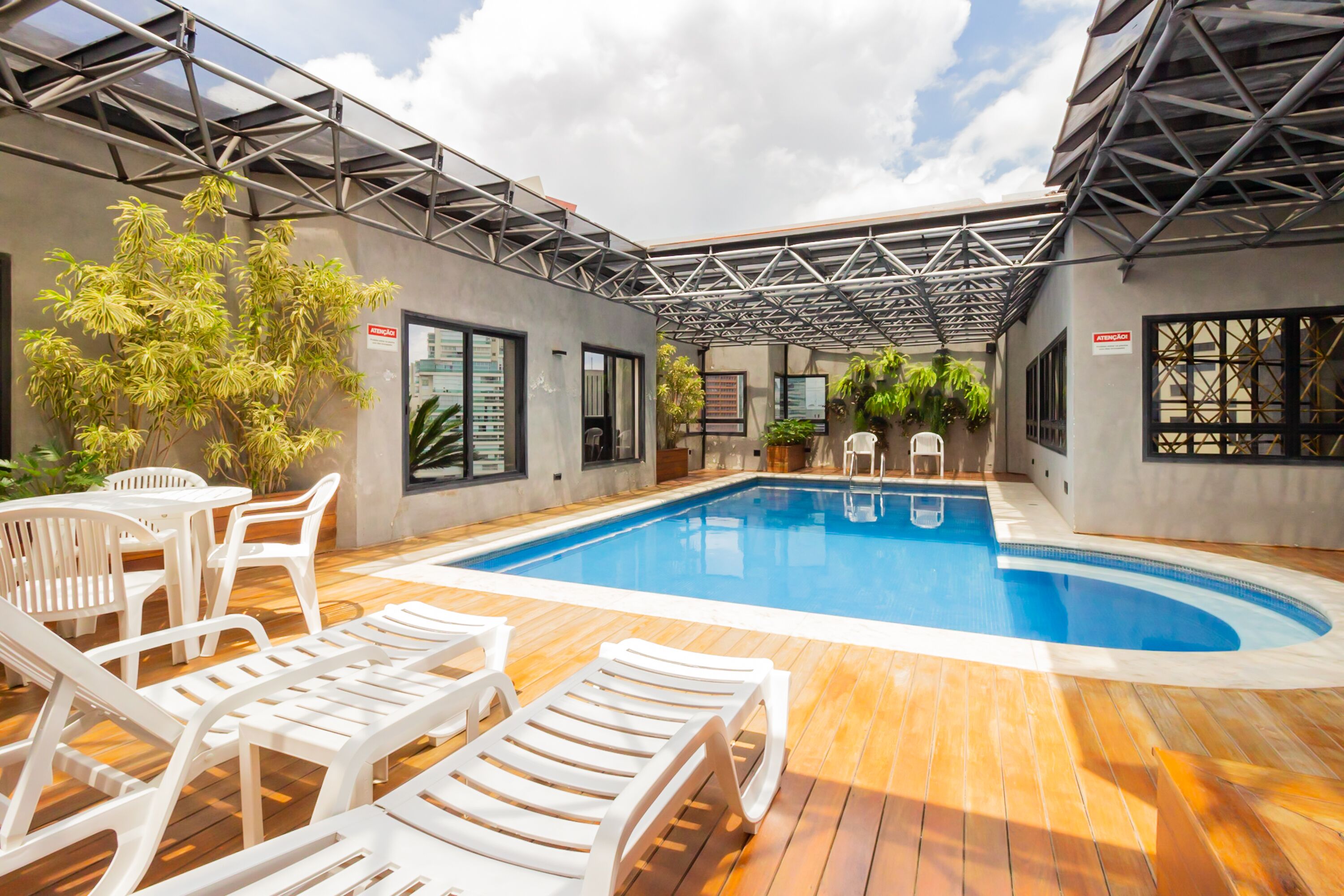 A modern outdoor pool area with lounge chairs, a wooden deck, and a metal roof structure.