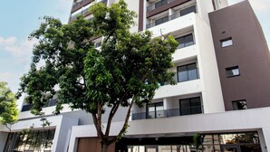 A high-rise building with multiple balconies, a parking area with cars, and a tree in front. - 360 SP Code (São Paulo)
