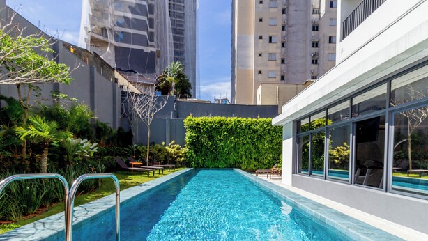 A rectangular swimming pool with metal handrails, surrounded by a landscaped garden with various plants and a hedge. - 360 SP Code (São Paulo)