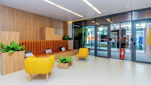 A modern reception area with a wooden wall, yellow chairs, and a seating area with cushions. - 360 SP Code (São Paulo)