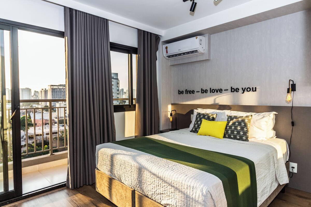 Ein modernes Hotelzimmer mit einem großen Bett, Blick auf die Stadt durch den Balkon und einem motivierenden Zitat an der Wand.