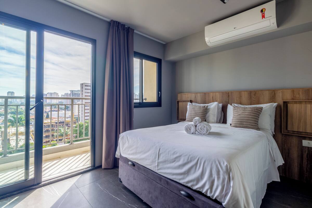 Ein Hotelzimmer mit einem großen Bett, Blick auf die Stadt und einer Klimaanlage.