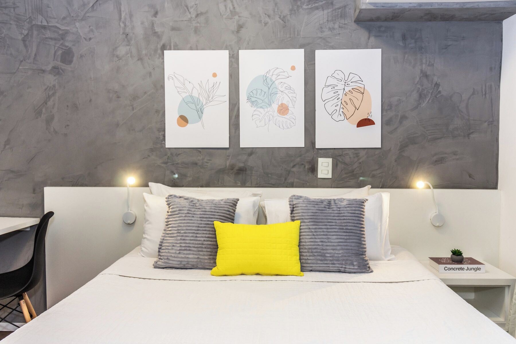 Een moderne slaapkamer met een bed, kussens en drie kunstwerken aan de muur.