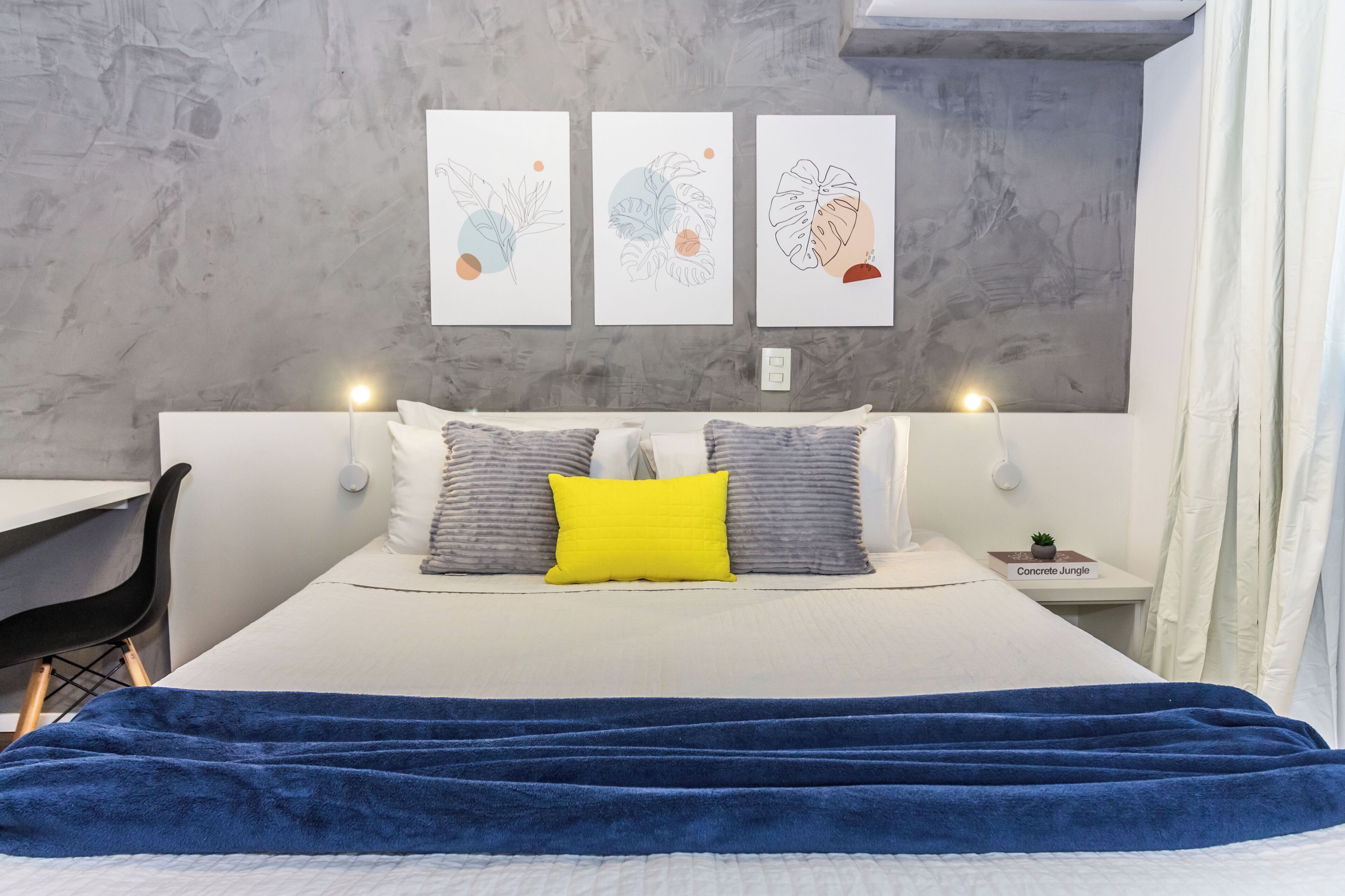 Un dormitorio moderno con una cama grande, un escritorio y una silla. Hay tres obras de arte colgadas en la pared sobre la cama.