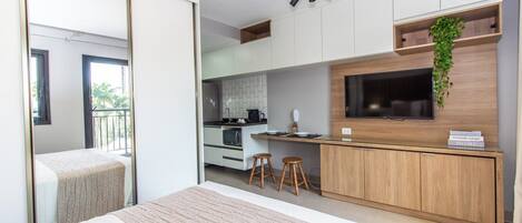 A modern hotel room with a large bed, a kitchenette, a TV, and a balcony.