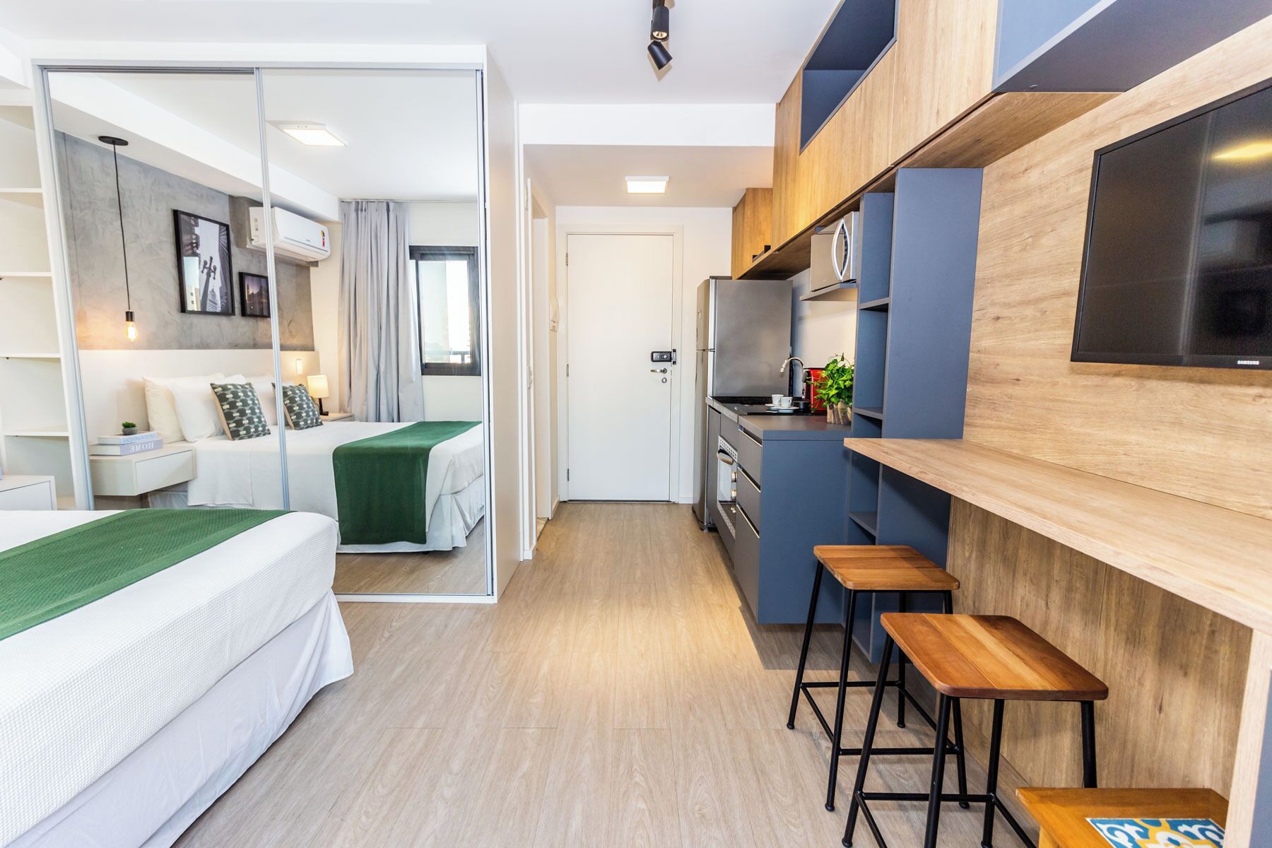 Une chambre d’hôtel moderne équipée d’un lit, d’une petite kitchenette et d’un coin salon avec des tabourets.