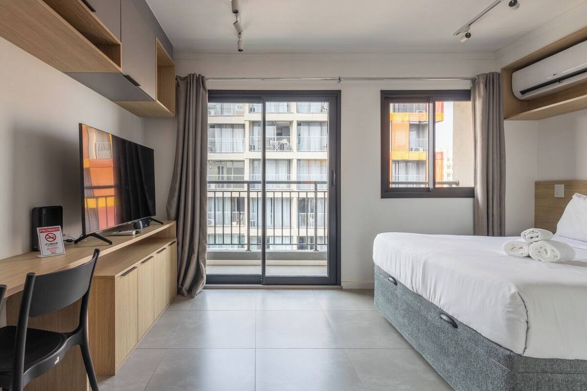 Ein Hotelzimmer mit Bett, Schreibtisch, Fernseher und einem Balkon mit Blick auf die Stadt.