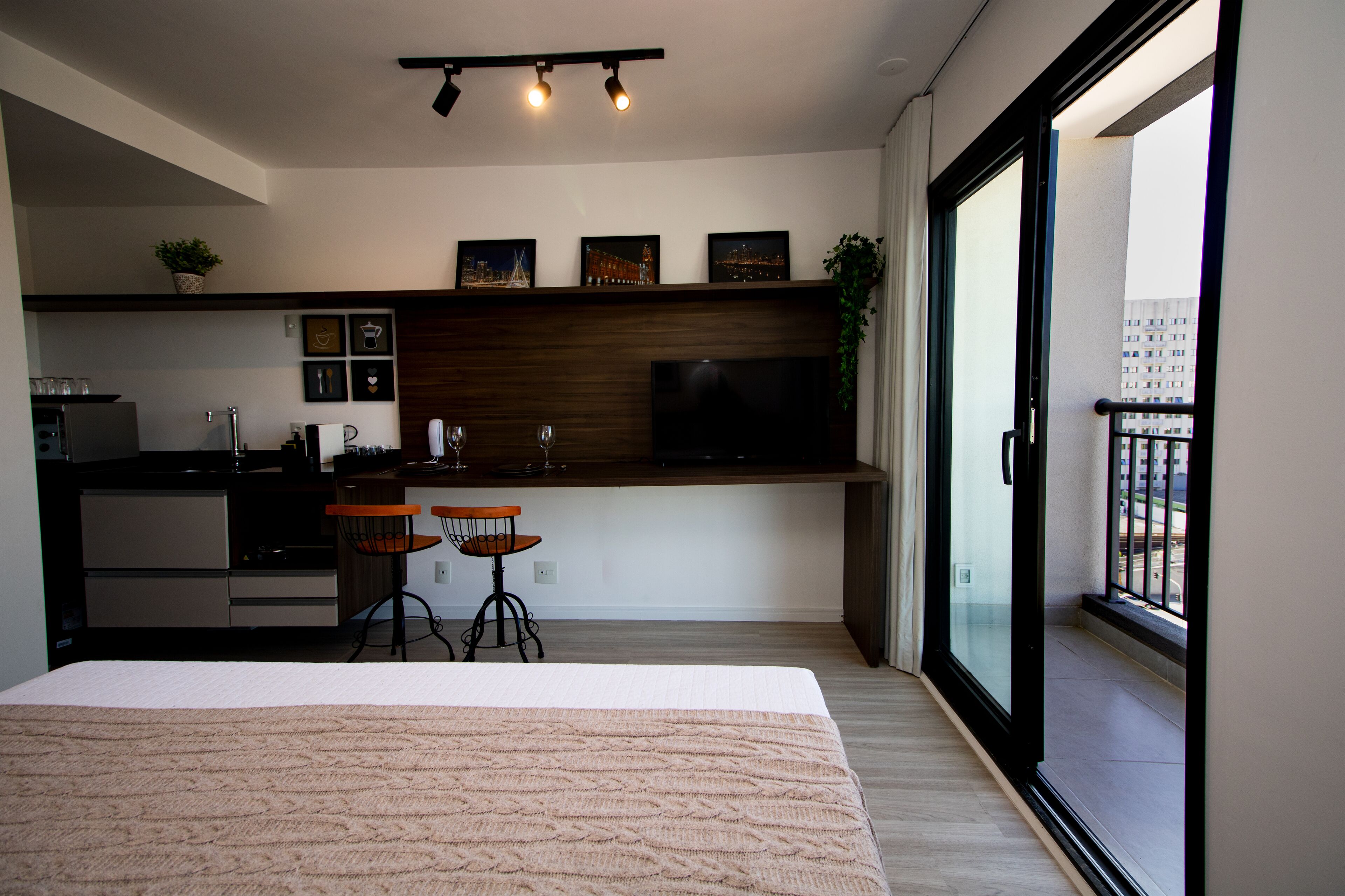 Un apartamento moderno con kitchenette, una zona de comedor con dos sillas, una cama grande y un balcón con vistas a la ciudad.