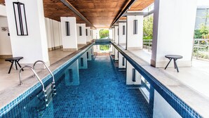 Ein moderner, überdachter Schwimmbereich mit Holzbalkendecke, weißen Wänden und blau gefliestem Boden.