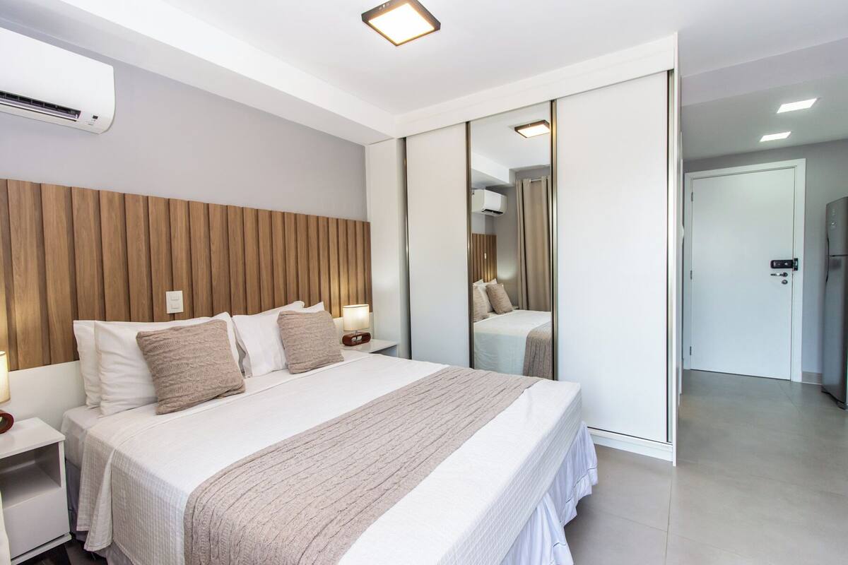 Ein modernes Hotelzimmer mit einem großen Bett, einem Holzkopfteil, einem Nachttisch mit Lampe und einer Schiebetür zu einem Badezimmer.